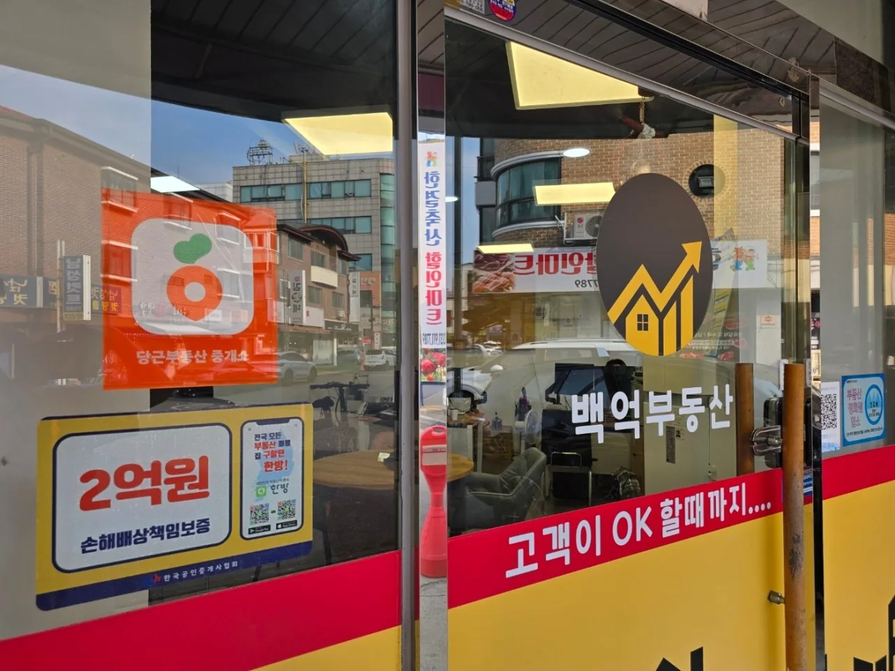 당근부동산 중개소 스티커와 손해배상 책임보증 안내가 붙은 백억부동산 유리문